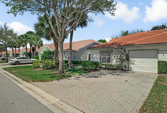 mediterranean / spanish home featuring decorative driveway, a tiled roof, an attached garage, and stucco siding