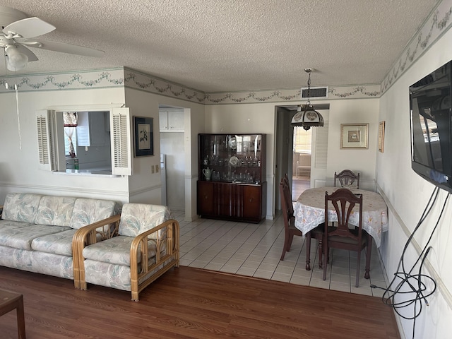 dining room with a ceiling fan, a textured ceiling, visible vents, and wood finished floors