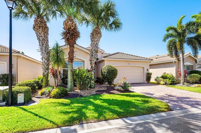 mediterranean / spanish-style home featuring a front yard, an attached garage, stucco siding, a tiled roof, and decorative driveway