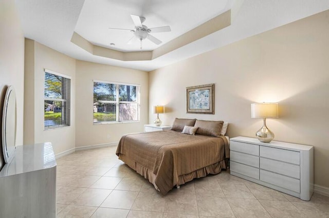 bedroom featuring light tile patterned floors, a tray ceiling, baseboards, and ceiling fan