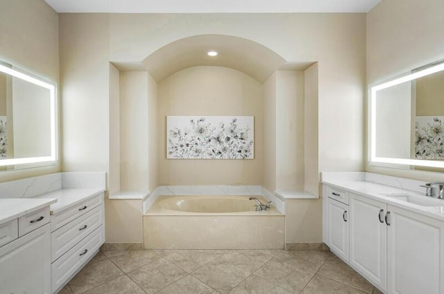 full bathroom featuring two vanities, a garden tub, and a sink