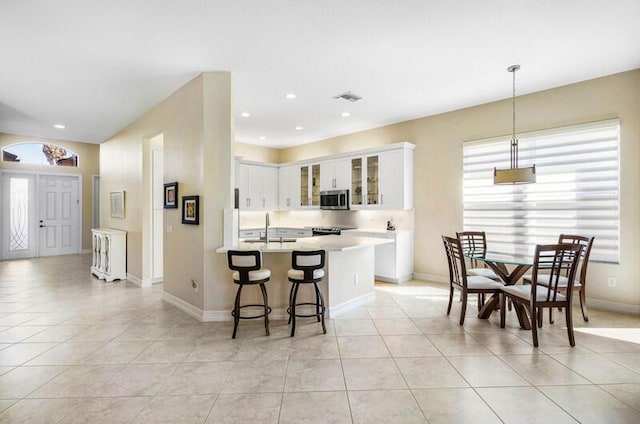 kitchen with stainless steel microwave, visible vents, light countertops, a kitchen breakfast bar, and light tile patterned flooring