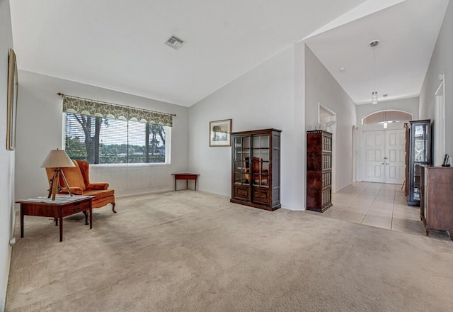 living area with high vaulted ceiling, visible vents, baseboards, and light carpet