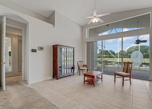 living area with ceiling fan, light tile patterned flooring, a water view, high vaulted ceiling, and arched walkways