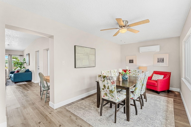 dining area with a textured ceiling, a wall unit AC, wood finished floors, and baseboards