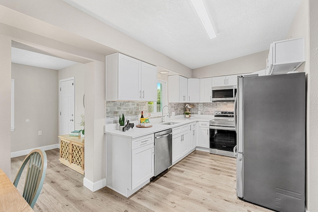 kitchen with light wood-style flooring, stainless steel appliances, a sink, white cabinets, and tasteful backsplash