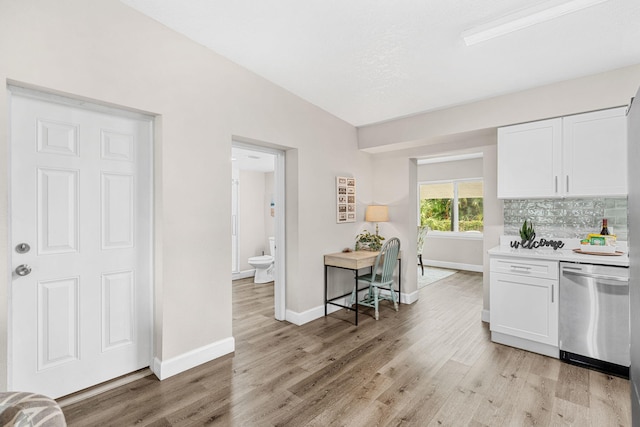 kitchen featuring light countertops, light wood-style flooring, decorative backsplash, stainless steel dishwasher, and white cabinets