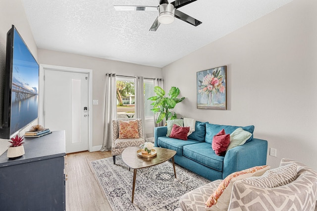 living area featuring light wood finished floors, baseboards, a ceiling fan, and a textured ceiling