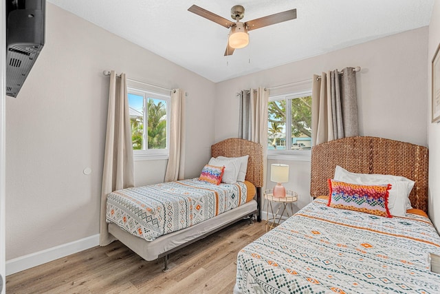 bedroom with multiple windows, light wood-type flooring, a ceiling fan, and baseboards