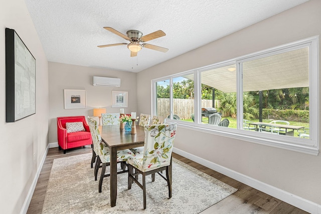 dining space featuring an AC wall unit, a textured ceiling, baseboards, and wood finished floors