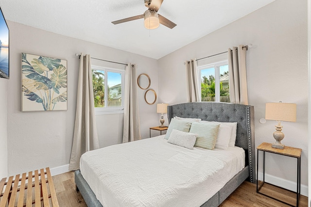 bedroom with a ceiling fan, multiple windows, baseboards, and wood finished floors