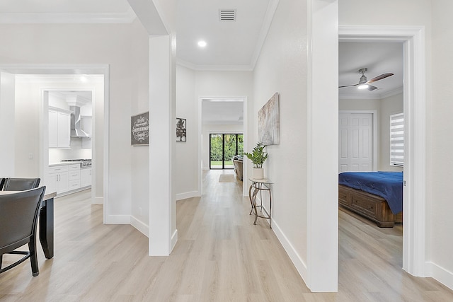 hallway featuring crown molding, baseboards, visible vents, and light wood finished floors