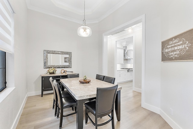 dining room featuring light wood finished floors, a raised ceiling, baseboards, and ornamental molding