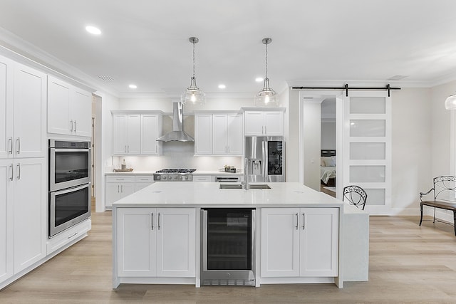 kitchen with ornamental molding, wine cooler, appliances with stainless steel finishes, a barn door, and wall chimney exhaust hood