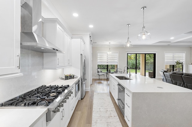 kitchen with stainless steel appliances, wall chimney exhaust hood, light countertops, and a sink