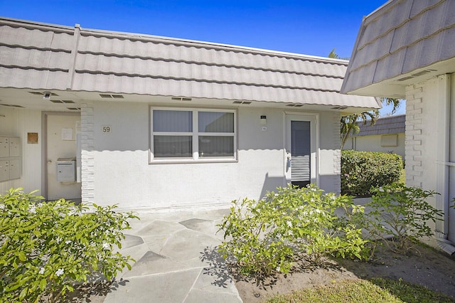 view of exterior entry with a tiled roof and stucco siding