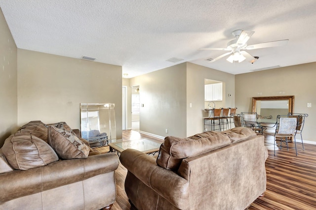 living room with wood finished floors, visible vents, baseboards, ceiling fan, and a textured ceiling