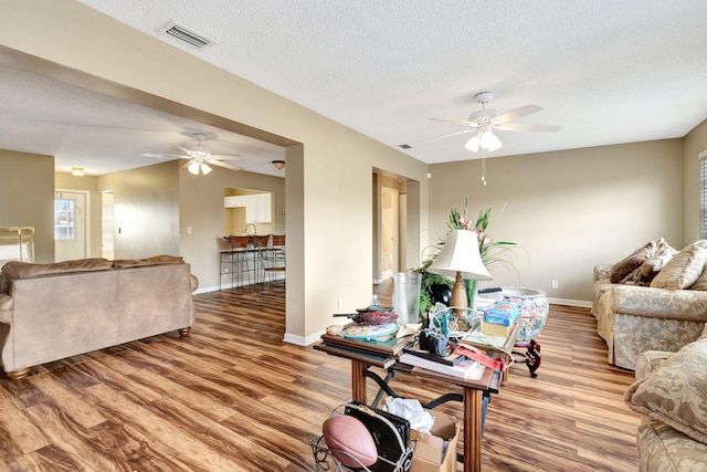 living room featuring ceiling fan, baseboards, a textured ceiling, and wood finished floors