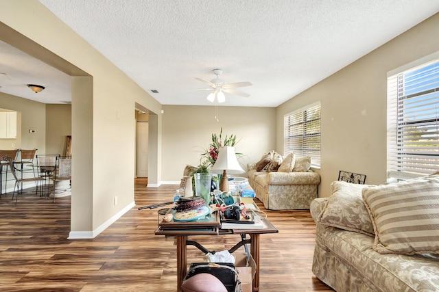 living area featuring ceiling fan, wood finished floors, baseboards, and a textured ceiling