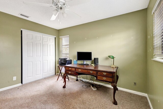 carpeted home office with a ceiling fan, baseboards, visible vents, and a textured ceiling