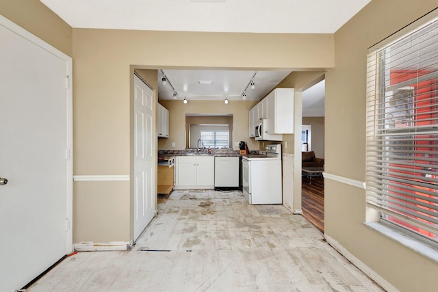 kitchen with white appliances, white cabinets, baseboards, and a sink