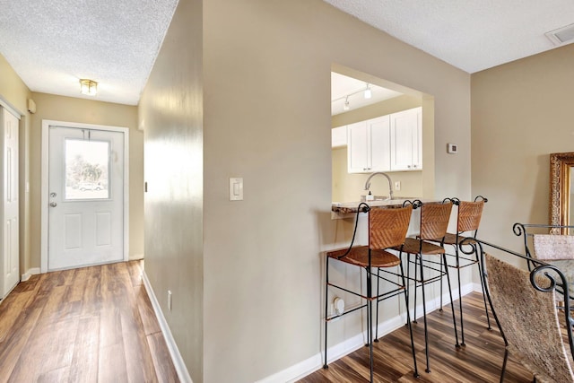 interior space with wood finished floors, baseboards, white cabinetry, a textured ceiling, and a kitchen bar