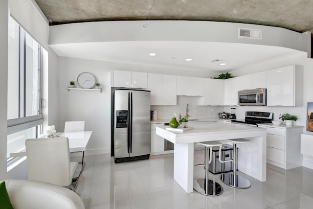 kitchen with stainless steel appliances, decorative backsplash, light countertops, white cabinets, and a kitchen bar