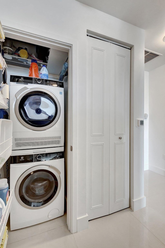 laundry area with tile patterned flooring, visible vents, baseboards, stacked washer and dryer, and laundry area