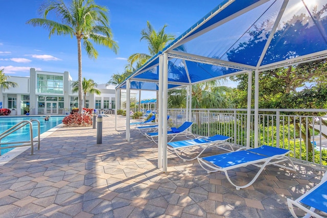 view of patio with a lanai, a community pool, and fence