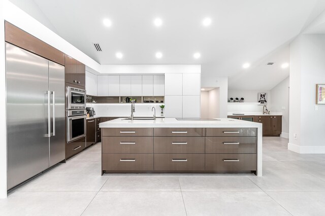 kitchen featuring a center island with sink, high vaulted ceiling, light countertops, built in appliances, and modern cabinets