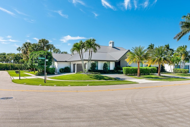 view of front of house featuring driveway, a chimney, a front lawn, a garage, and metal roof