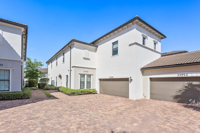 view of front of home with stucco siding, a tile roof, a garage, and decorative driveway
