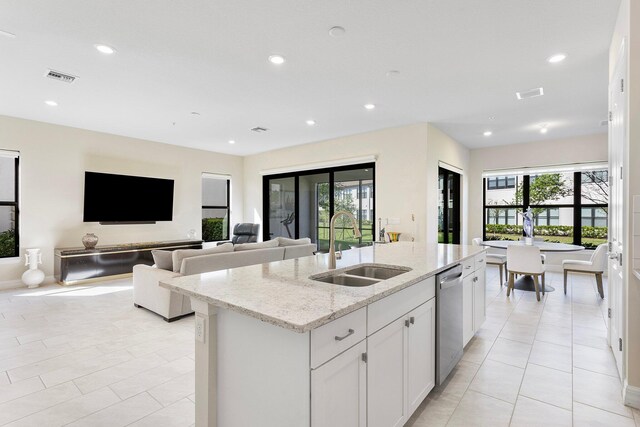 kitchen with visible vents, a center island with sink, a sink, light stone counters, and stainless steel dishwasher