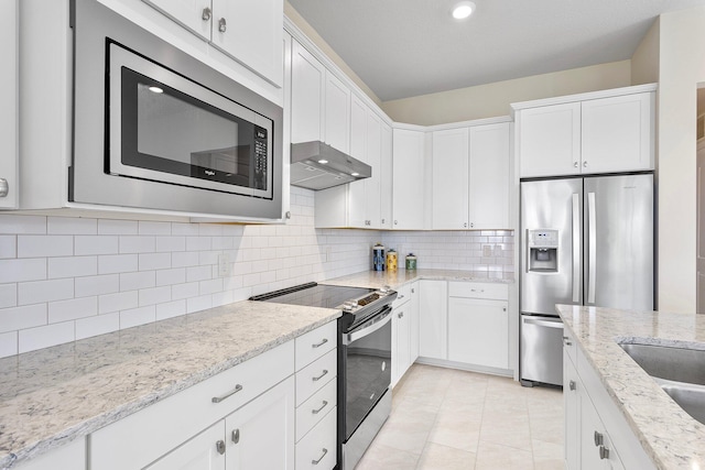 kitchen featuring light stone countertops, stainless steel appliances, under cabinet range hood, white cabinetry, and backsplash