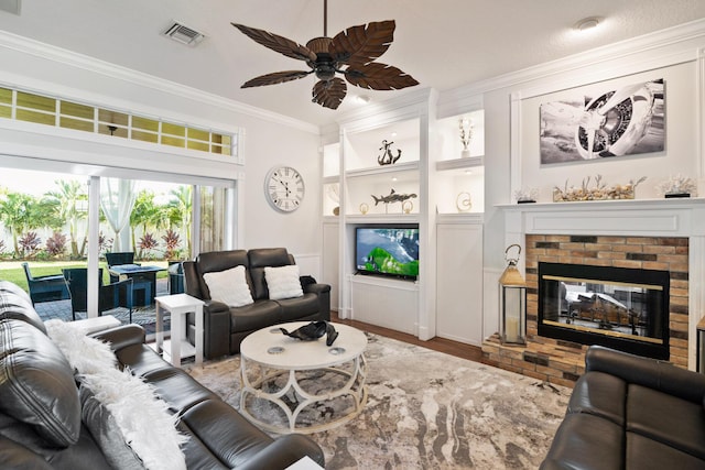 living room featuring built in features, visible vents, a ceiling fan, crown molding, and a fireplace