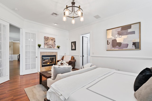 bedroom with crown molding, a fireplace, visible vents, and wood finished floors