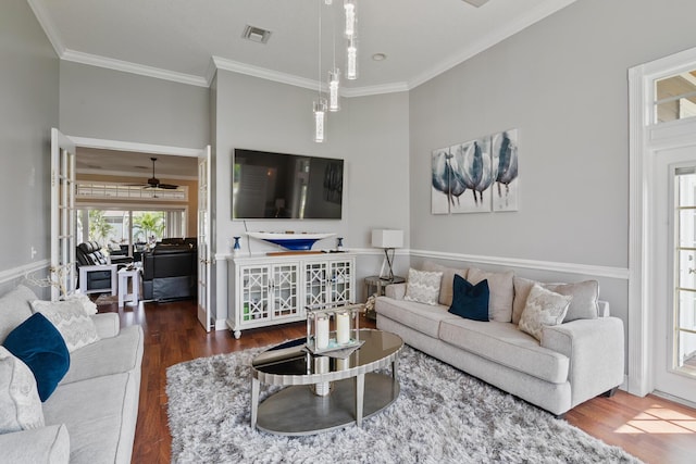 living area with ornamental molding, wood finished floors, visible vents, and a ceiling fan