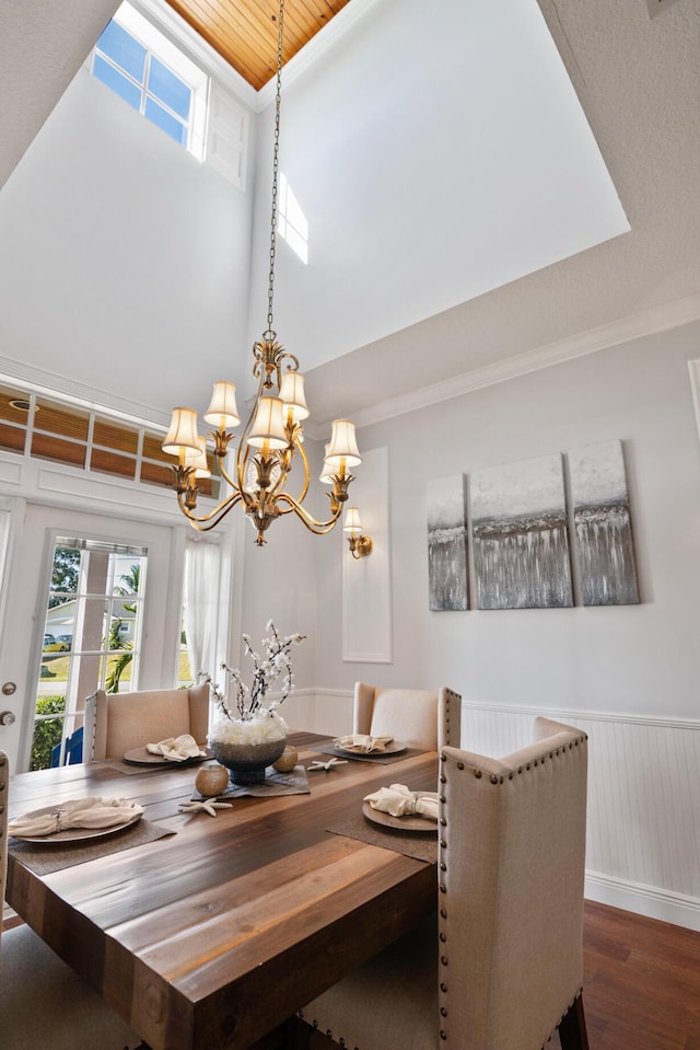 dining room with a towering ceiling, ornamental molding, wainscoting, wood finished floors, and a chandelier