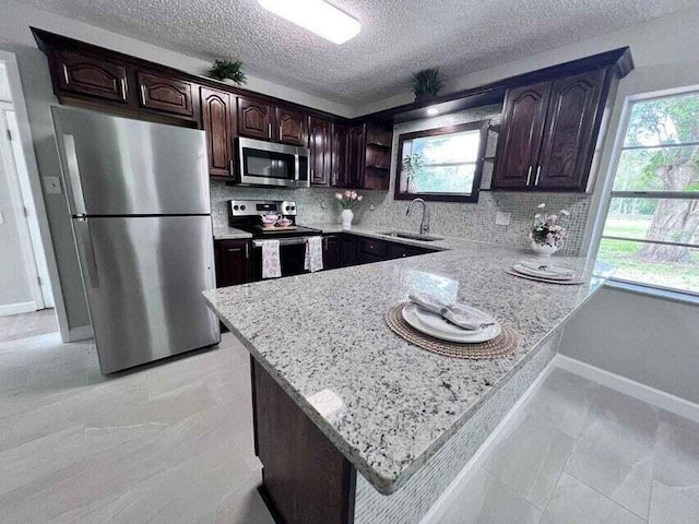 kitchen with dark brown cabinetry, tasteful backsplash, a peninsula, stainless steel appliances, and a sink