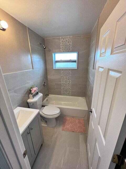 full bath with bathing tub / shower combination, toilet, tile patterned floors, vanity, and tile walls