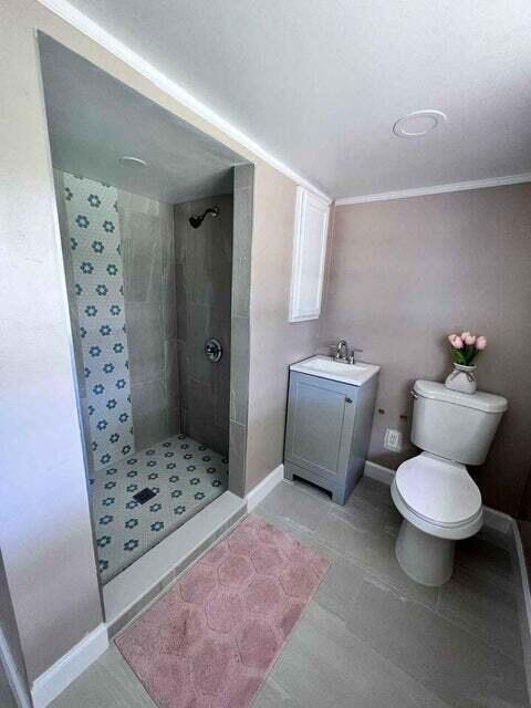 bathroom with baseboards, a tile shower, vanity, and toilet