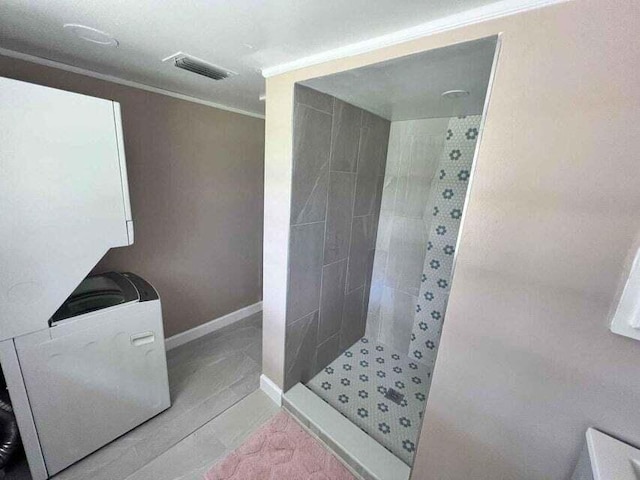 full bath featuring visible vents, crown molding, a tile shower, and baseboards