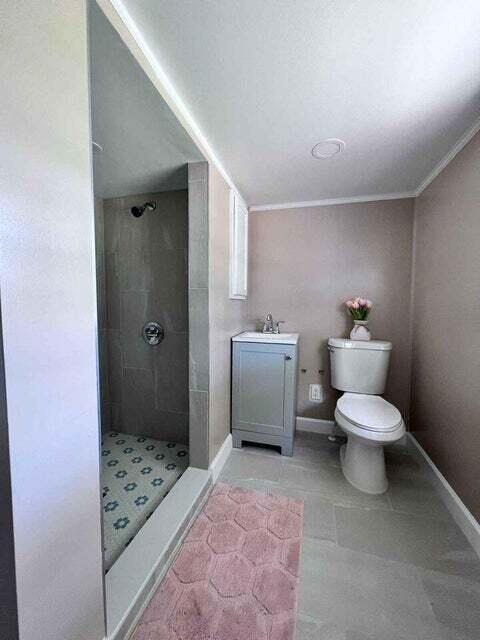 bathroom with tiled shower, vanity, toilet, and baseboards