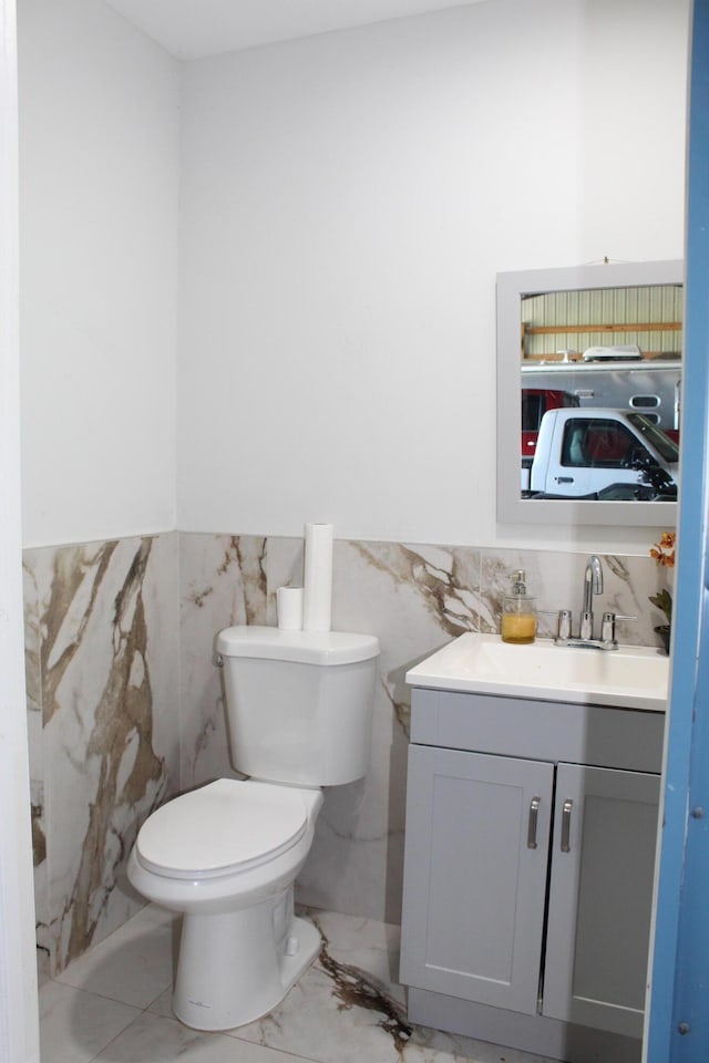 bathroom featuring toilet, a wainscoted wall, vanity, tile walls, and marble finish floor