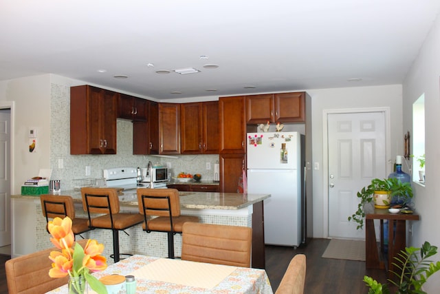 kitchen featuring dark wood finished floors, decorative backsplash, freestanding refrigerator, range, and a peninsula