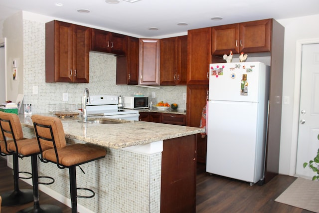 kitchen featuring a peninsula, white appliances, dark wood-style flooring, a sink, and decorative backsplash