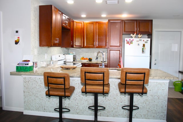 kitchen with white appliances, decorative backsplash, dark wood-style flooring, a peninsula, and a sink