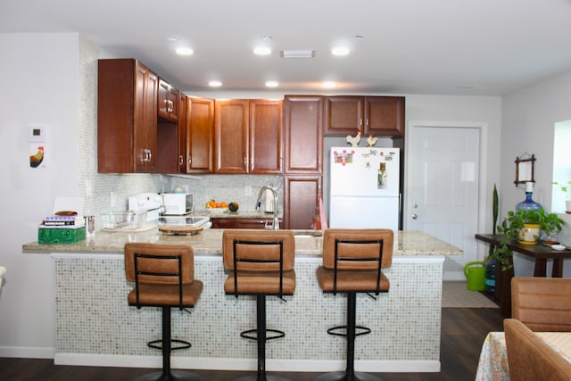 kitchen with a breakfast bar, decorative backsplash, dark wood-type flooring, freestanding refrigerator, and a peninsula