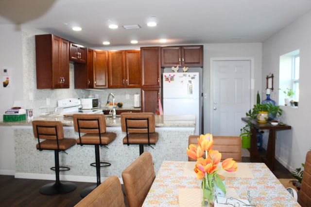 kitchen with dark wood-style floors, backsplash, a sink, white appliances, and a peninsula