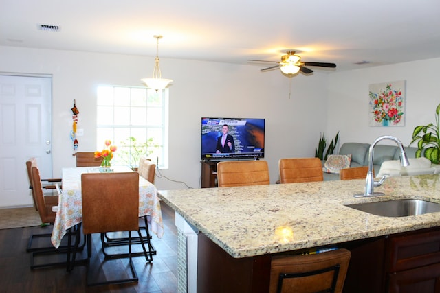 kitchen with light stone counters, dark wood-type flooring, a sink, visible vents, and decorative light fixtures